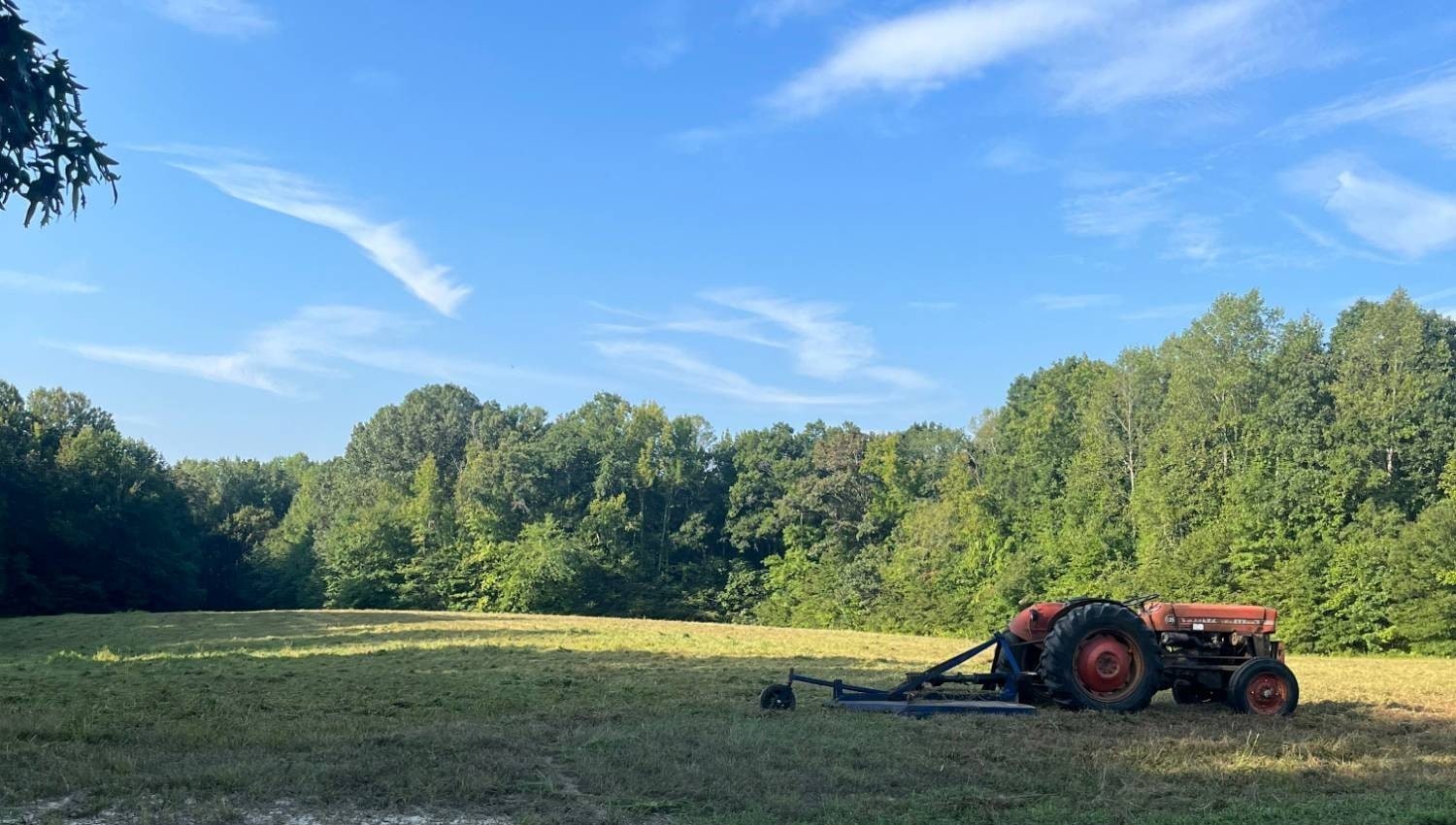A bushhog tractor at the edge of a freshly cut Virginia hay field, blue summer sky overhead — the country Bield is built in and built for.